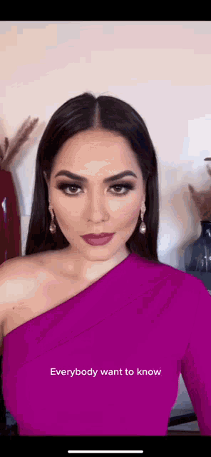 a woman wearing a pink one shoulder dress and earrings is standing in front of a vase .