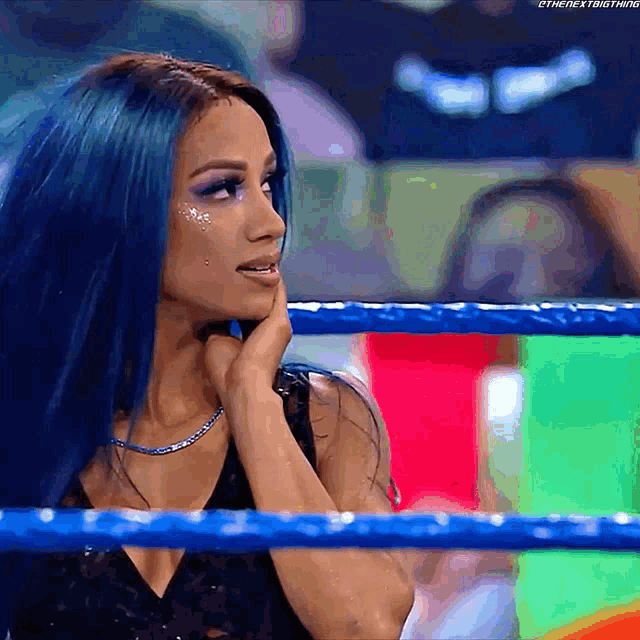 a woman with blue hair is standing in a wrestling ring with her hand on her chin