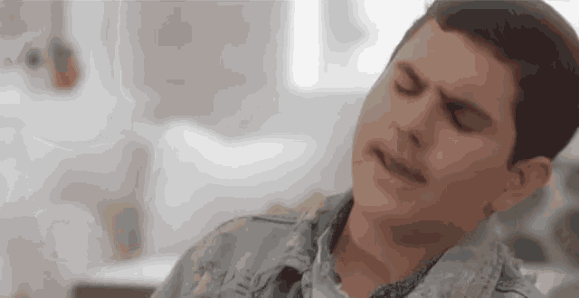 a young man in a denim jacket is singing into a microphone while sitting on a couch .