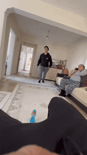 a man standing in a living room with a woman sitting on a couch behind him