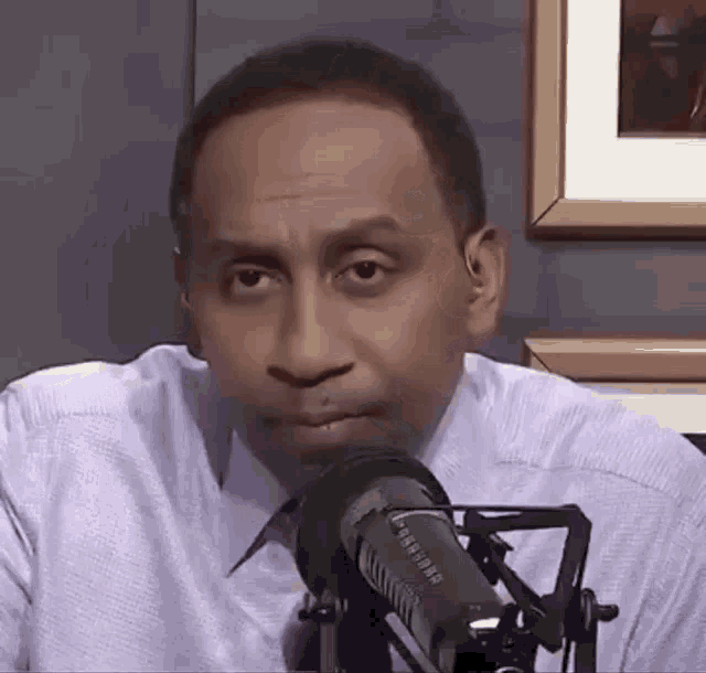 a man in a white shirt is sitting in front of a microphone and looking at the camera