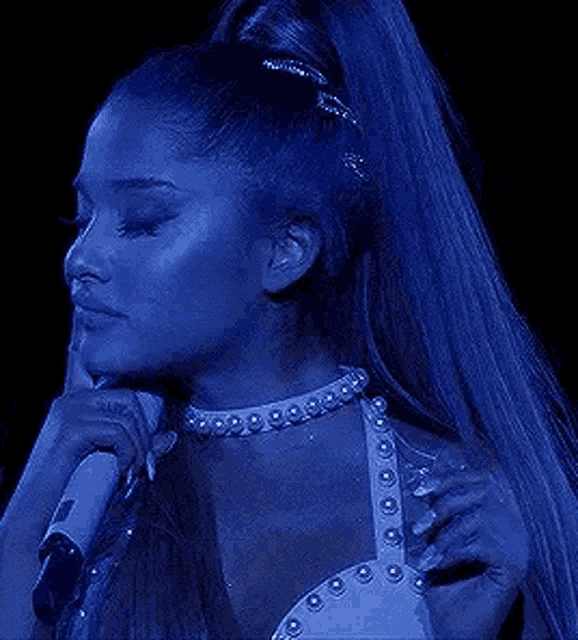 ariana grande is wearing a choker and holding a microphone while singing .