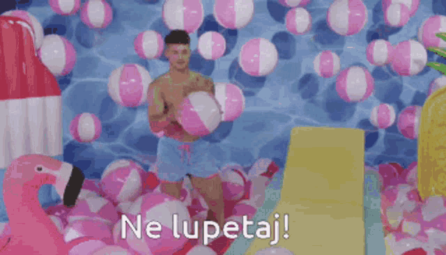a man standing in a pool surrounded by pink and white beach balls