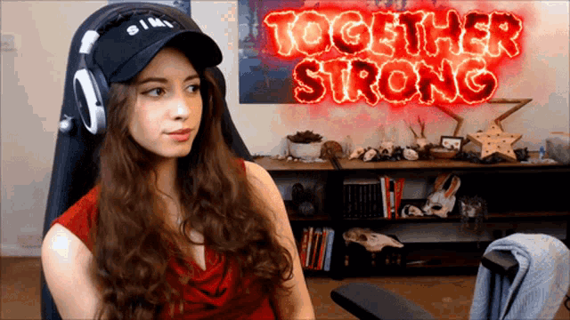 a woman wearing headphones sits in front of a neon sign that says together strong