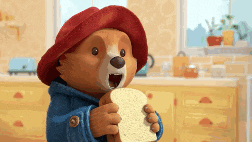paddington bear is eating a piece of bread in a kitchen