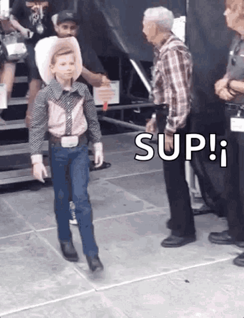 a young boy dressed as a cowboy is walking on a stage while a man stands behind him .