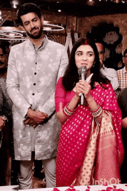 a woman in a pink dress is speaking into a microphone while standing next to a man in a suit