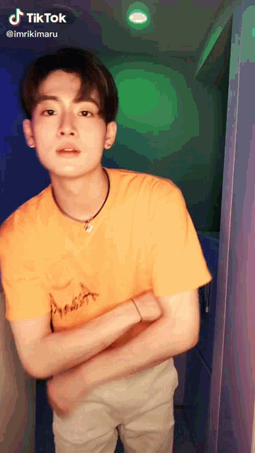 a young man wearing a yellow t-shirt is standing with his arms crossed and a tiktok icon above his head