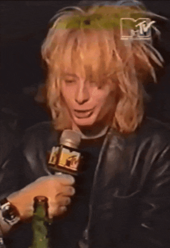 a man with long blonde hair is holding a microphone with a mtv logo behind him