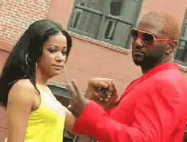 a man in a red suit is holding a woman 's hand in front of a brick building .