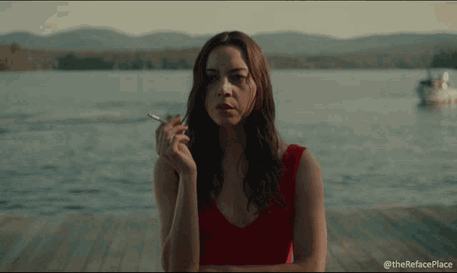 a woman in a red top is smoking a cigarette in front of a body of water