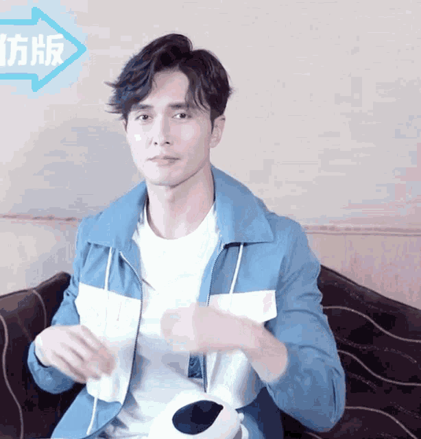 a man in a blue jacket sits on a couch with chinese writing on the wall behind him