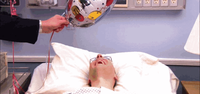 a man is laying in a hospital bed with a birthday balloon on his head