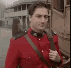 a man in a red uniform is standing in front of a building holding a gun .