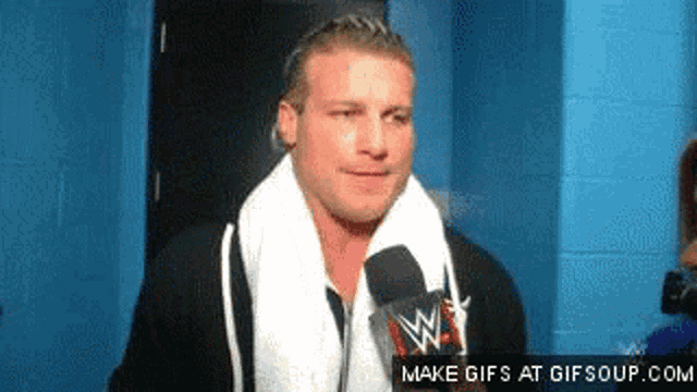 a wrestler with a towel around his neck is talking into a microphone ..