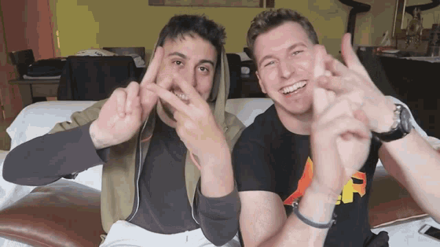 two men are making a peace sign with their hands and smiling