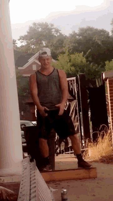 a man wearing a tank top and shorts is standing on a porch