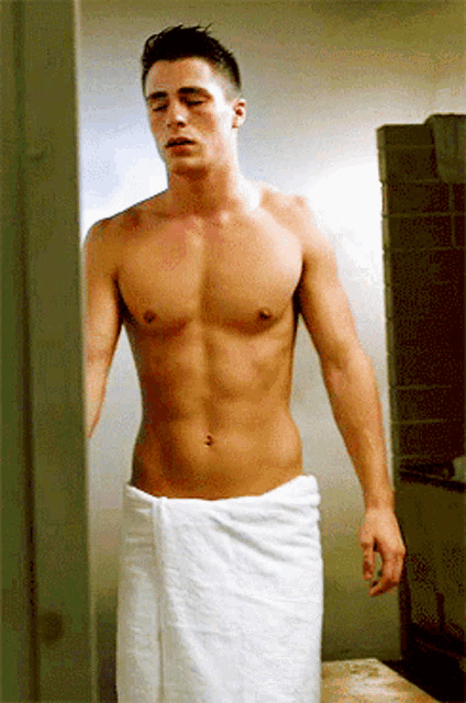 a shirtless man wrapped in a white towel standing in a bathroom