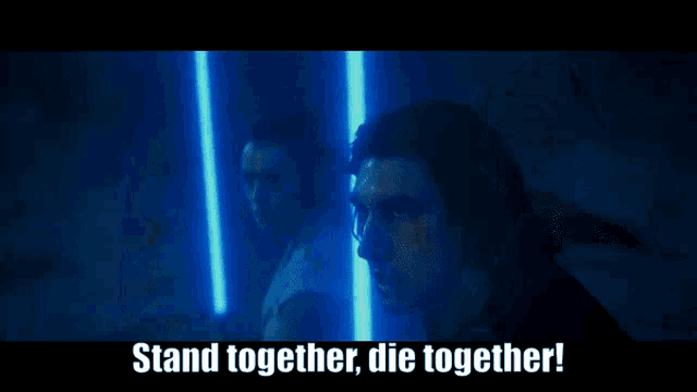 two men are standing next to each other in a dark room with lightsabers in their hands .