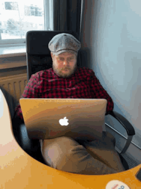 a man in a plaid shirt is sitting at a desk with an apple laptop