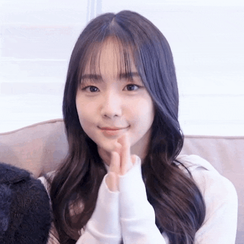 a young girl is sitting on a couch making a heart with her hands