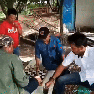 a man wearing a beatle shirt is playing chess with other men