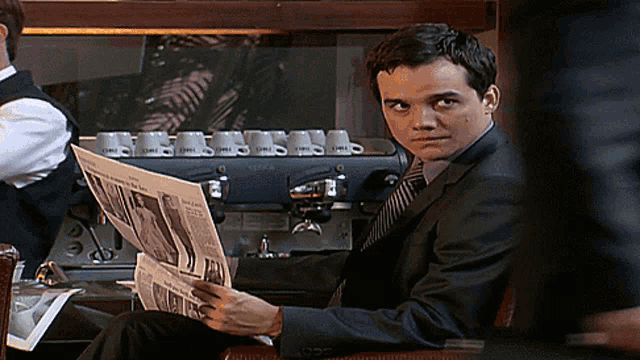 a man in a suit reads a newspaper in front of a coffee machine