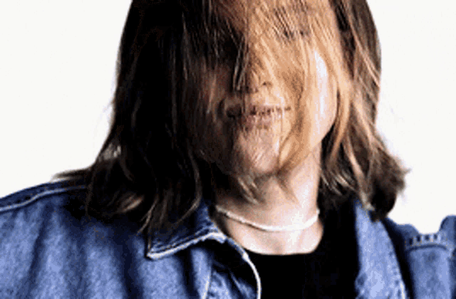 a woman wearing a denim jacket and a black shirt has her hair blowing in the wind