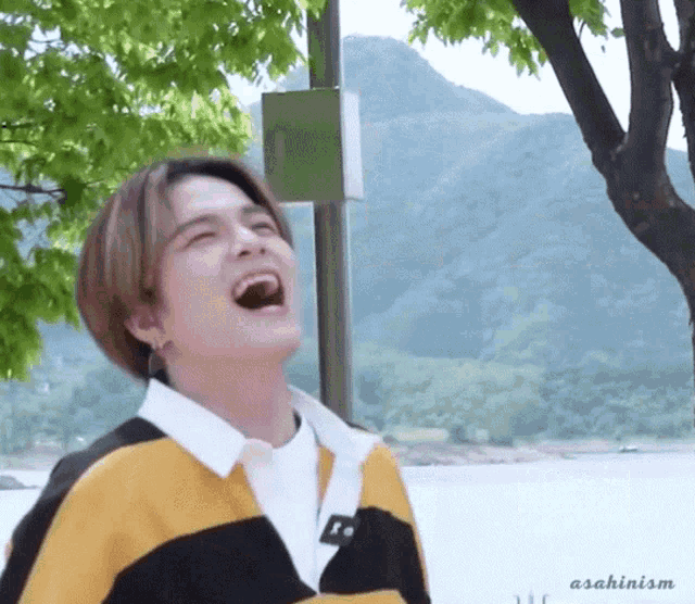 a young man is laughing with his mouth open while wearing a yellow and black sweater .