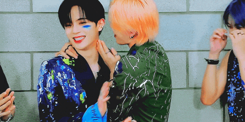 two men are hugging each other in front of a brick wall . one of the men has blue paint on his face .