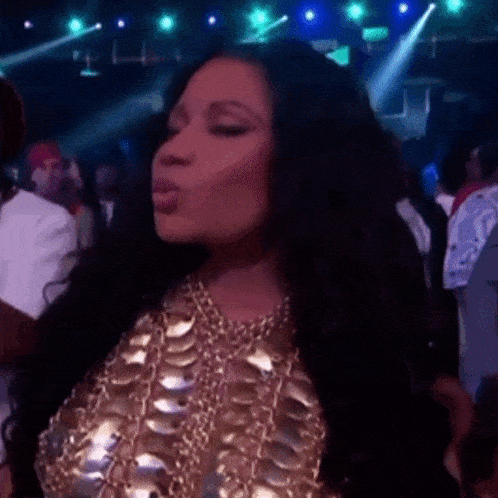 a woman wearing a gold top and necklace is blowing a kiss
