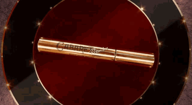 a gold tube of mascara is sitting on top of a red circle