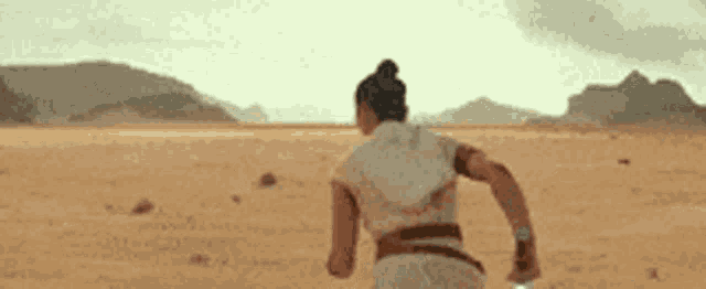 a person is running through a desert holding a light saber .