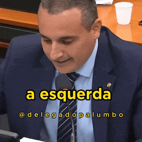 a man in a suit and tie is sitting in front of a microphone with the words a esquerda on the bottom