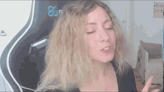 a woman with blonde hair is sitting in a chair with her eyes closed and making a funny face .