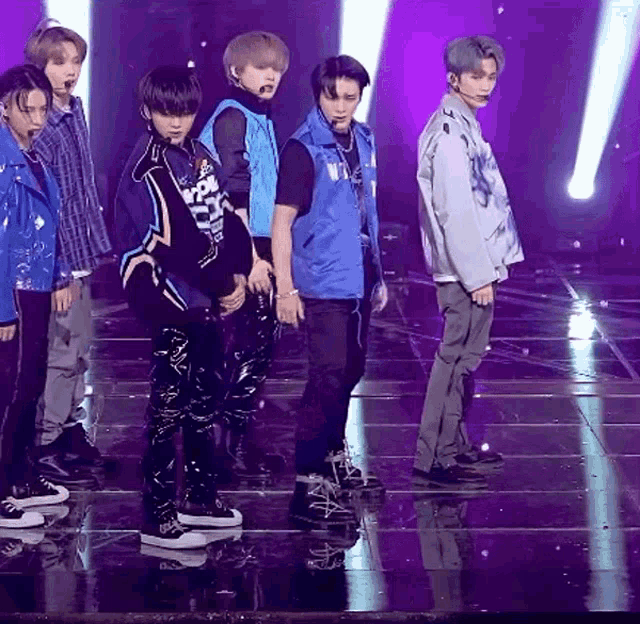a group of people standing on a stage with one wearing a vest that says ' nct ' on it
