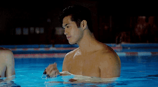 a shirtless man is standing in a swimming pool looking at something