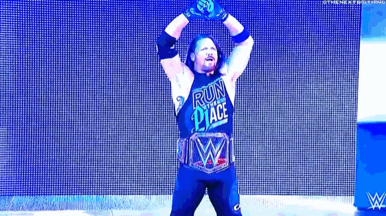 a wrestler is standing on a stage with his arms in the air and a wrestling belt .