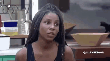 a woman with dreadlocks is sitting at a table in a kitchen with a bowl on it .