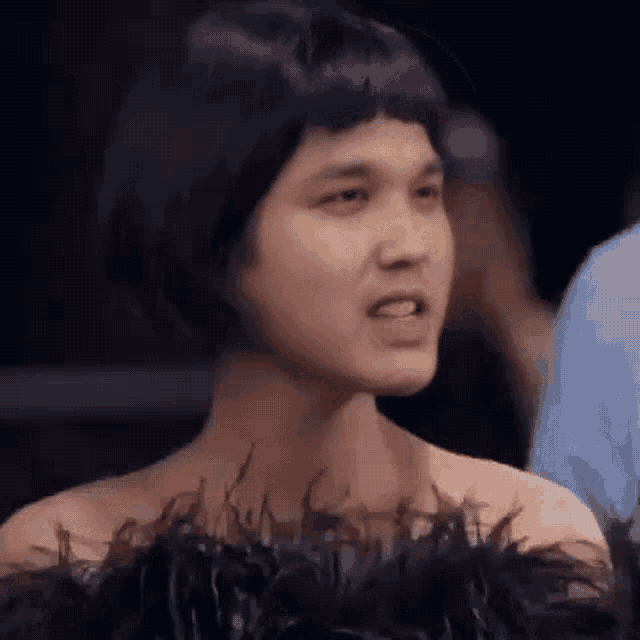 a man wearing a feathered dress and a wig is making a face .