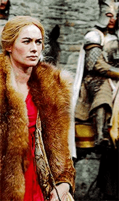 a woman wearing a fur coat and a red dress is standing in front of a man in armor .