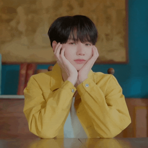 a young man in a yellow jacket rests his face on his hands