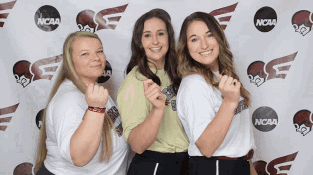 three girls are posing for a picture in front of a ncaa banner