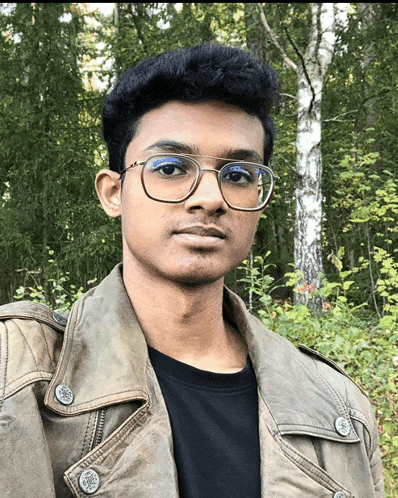 a man wearing glasses and a leather jacket stands in front of trees