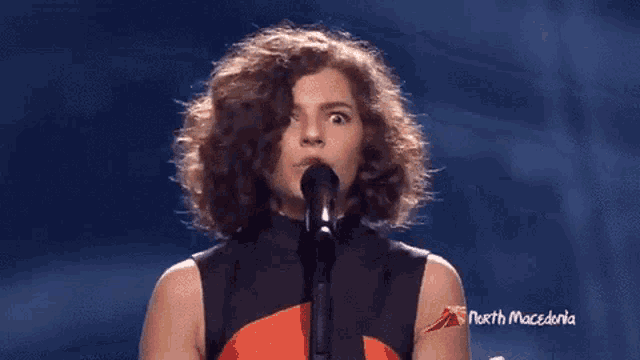 a woman singing into a microphone with a north macedonia logo in the corner