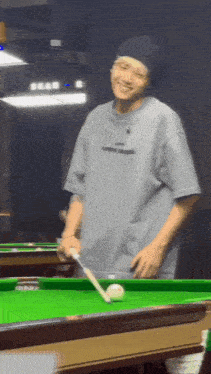 a man is standing next to a pool table holding a pool cue and smiling .