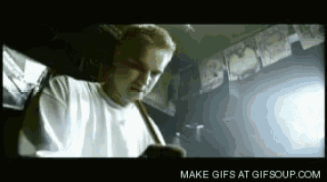 a man in a white shirt is sitting in a dark room looking at his phone .