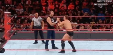 two men are wrestling in a ring with a referee in the background .