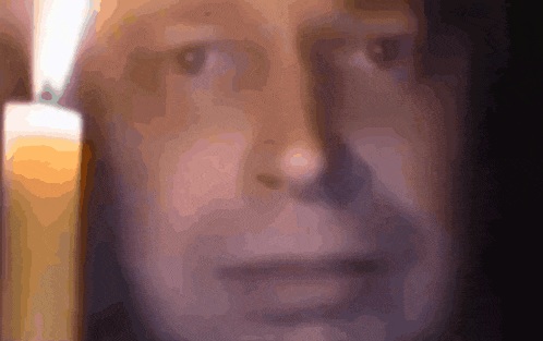 a close up of a man 's face with a lit candle behind him