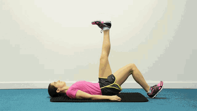 a woman in a pink shirt and black shorts is doing exercises on a mat